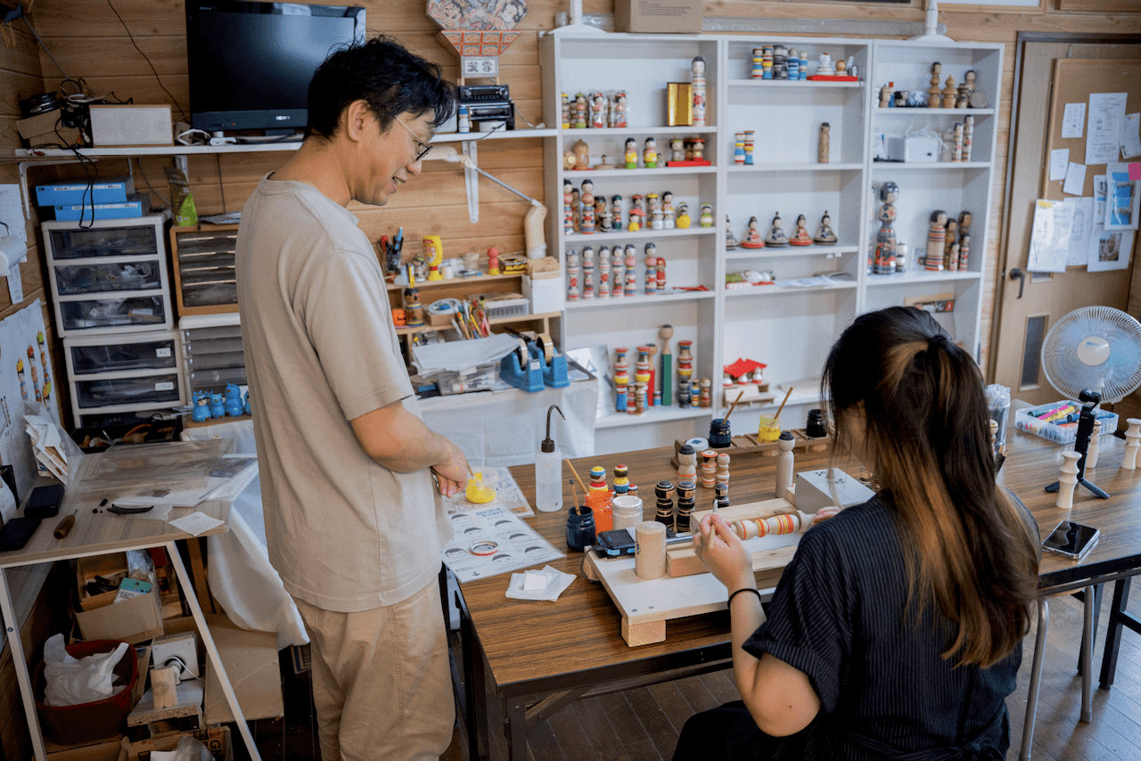Craftsman guiding someone making a kokeshi doll