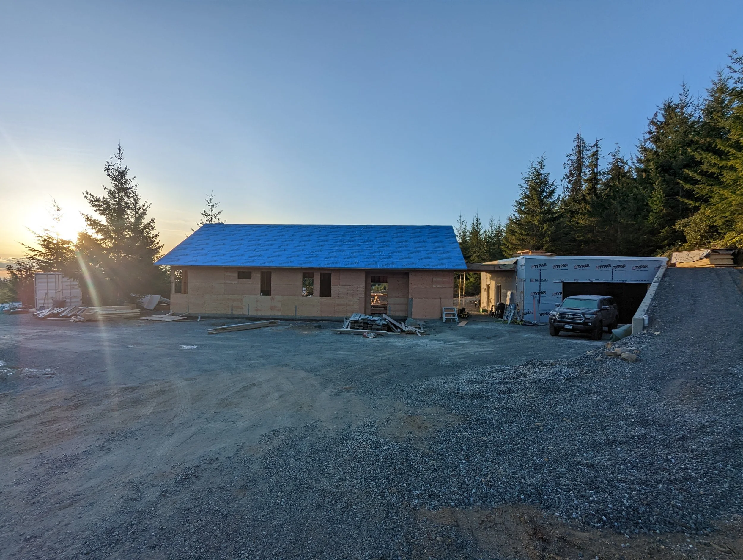 Modern two-story home with large glass windows, warmly lit interiors, and a balcony. Surrounded by trees and a manicured lawn at dusk. Cozy ambiance.