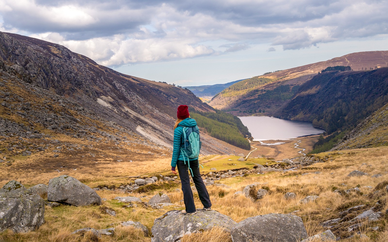 Person hiking in Glendalough National Park, overlooking Wicklow Mountains and lake.