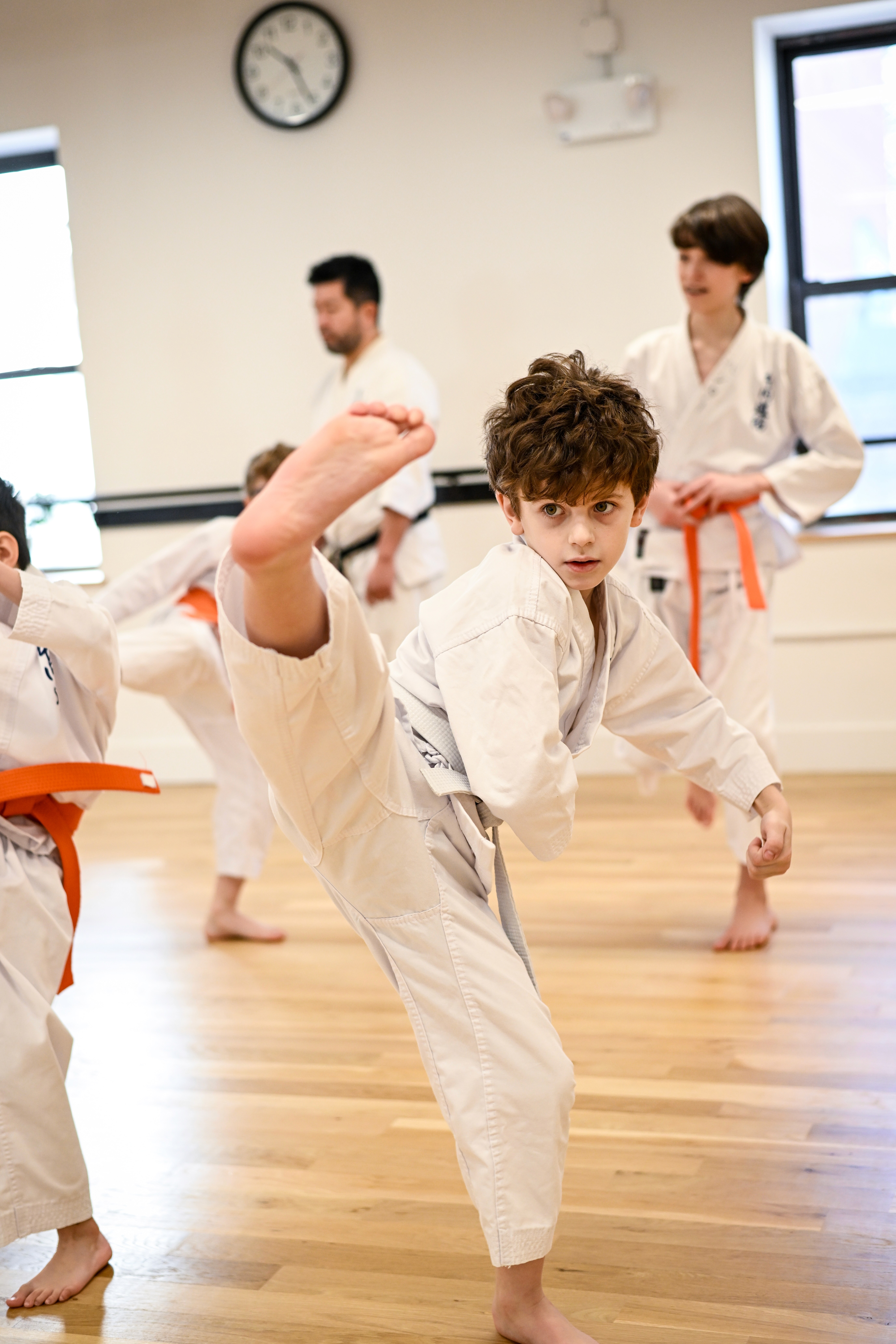 Person with a mustache wearing a black t-shirt carrying a tall stack of pizza boxes inside a dimly lit bar or restaurant.