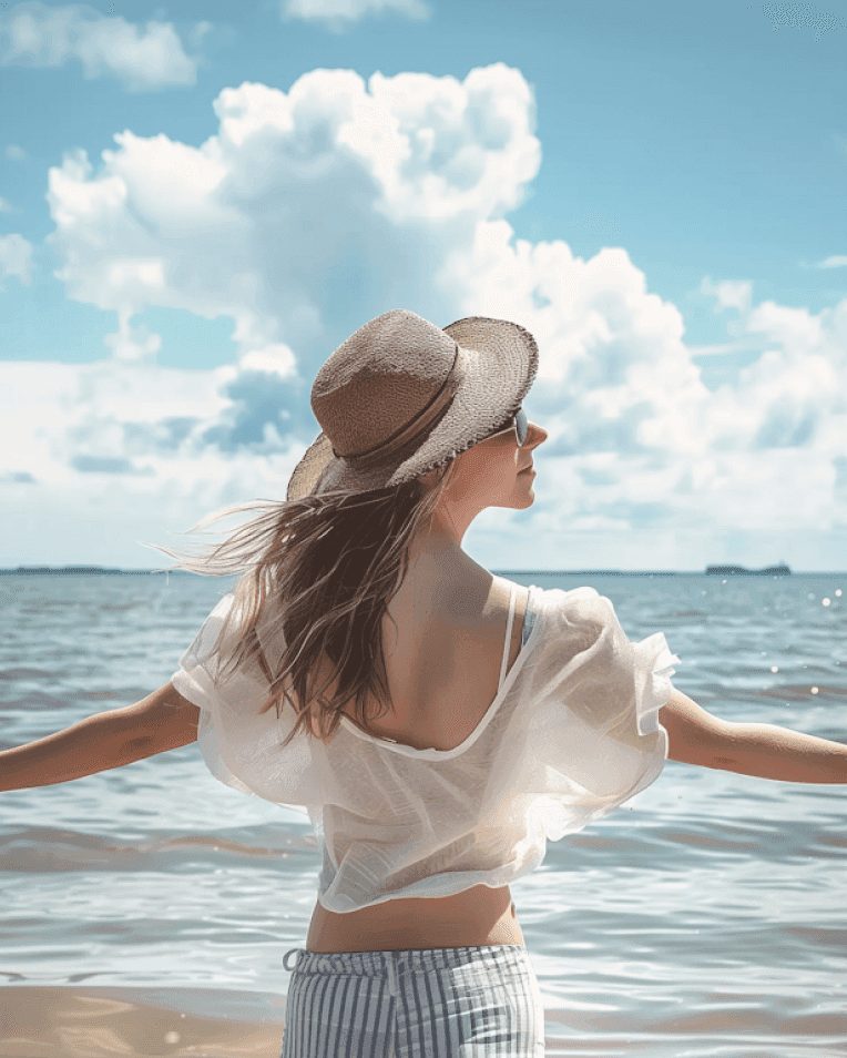 Woman in hat enjoying a sunny day by the sea with arms outstretched.