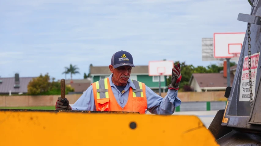 Asphalt screedman directing dumptruck to paving machine for hot mix asphalt material refill