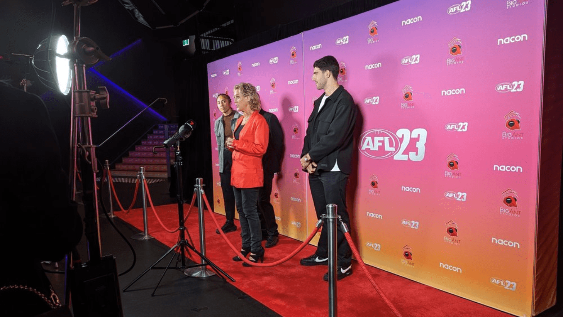 3 people standing on a red carpet in front of a media wall at Fortress