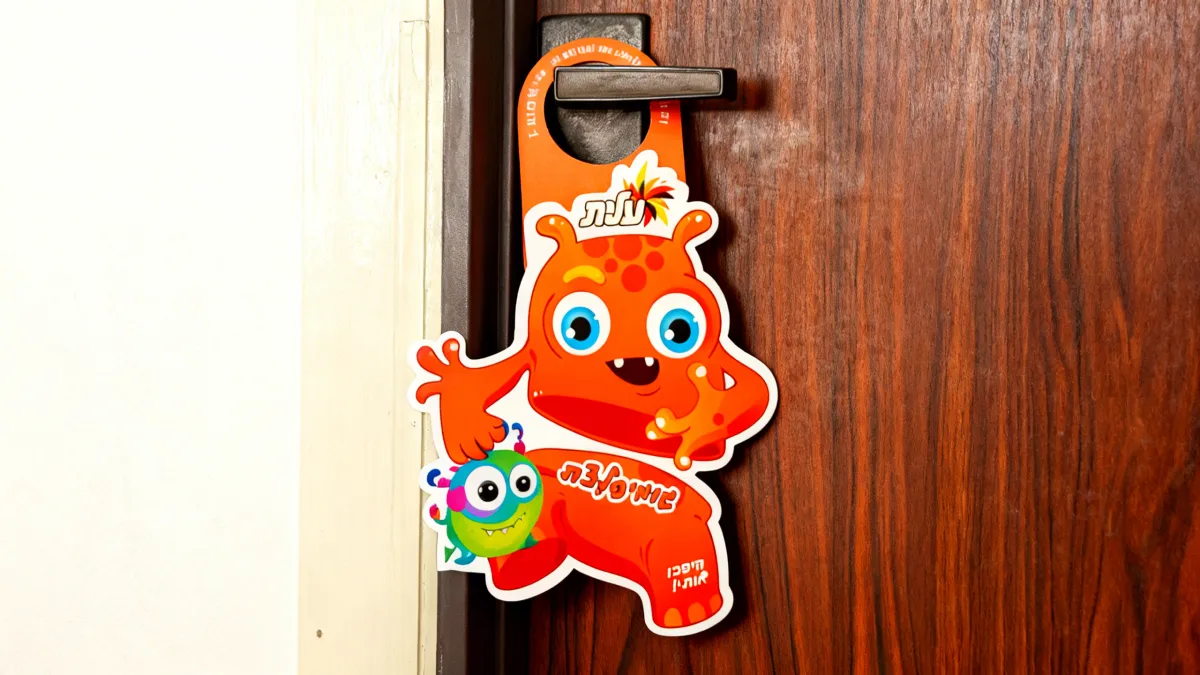 תלי-דלת מעוצב וצבעוני של חברת שטראוס עלית לפרסום מוצר סוכריות הגומי: גומיפלצת הפצה שבוצעה על ידי חברת עלונים על ידית הדלת. דוגמה לשירות הפצה יצירתי המיועד למשוך את תשומת לב הדיירים באופן מיידי ובולט.