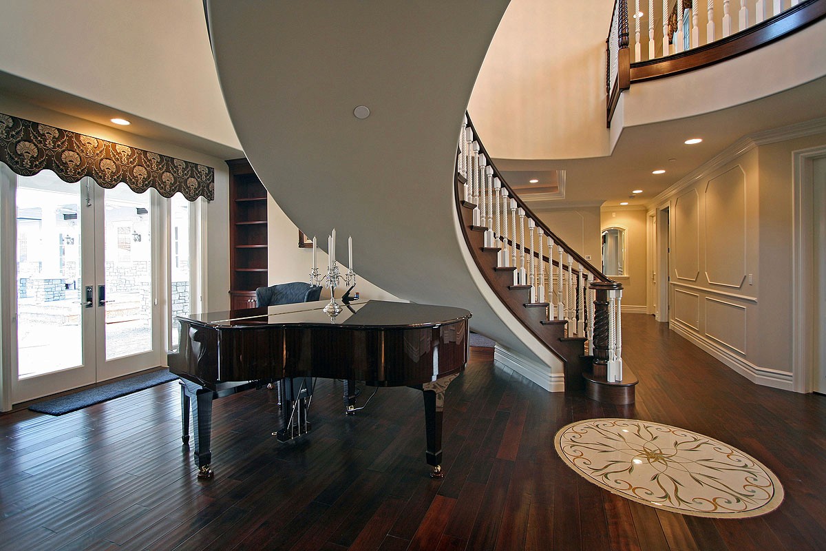 Curved, freestanding staircase with a piano placed underneath, emphasizing the unique design of the space.