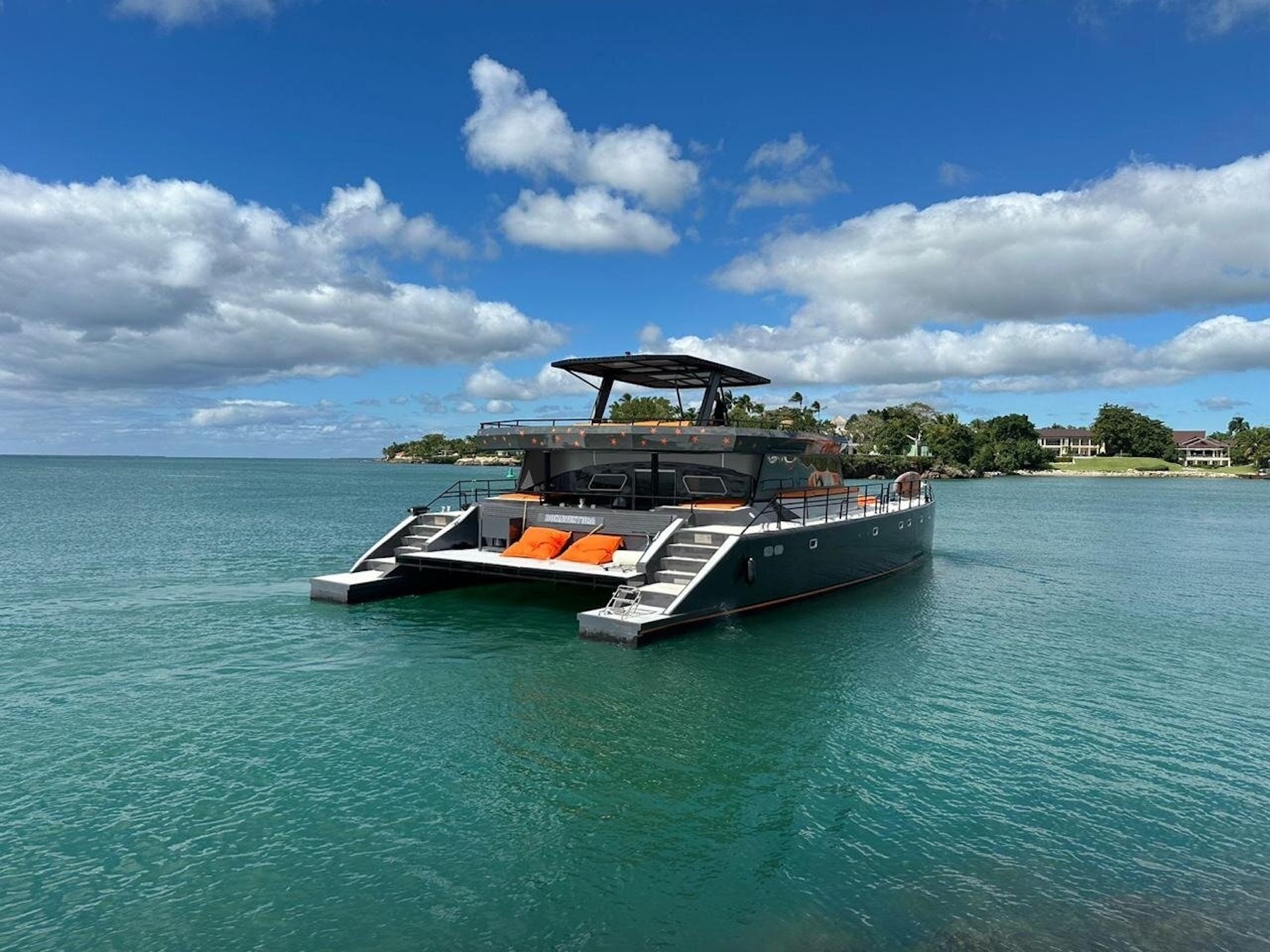 Modern catamaran anchored in calm turquoise water near a tropical shoreline under scattered clouds.
