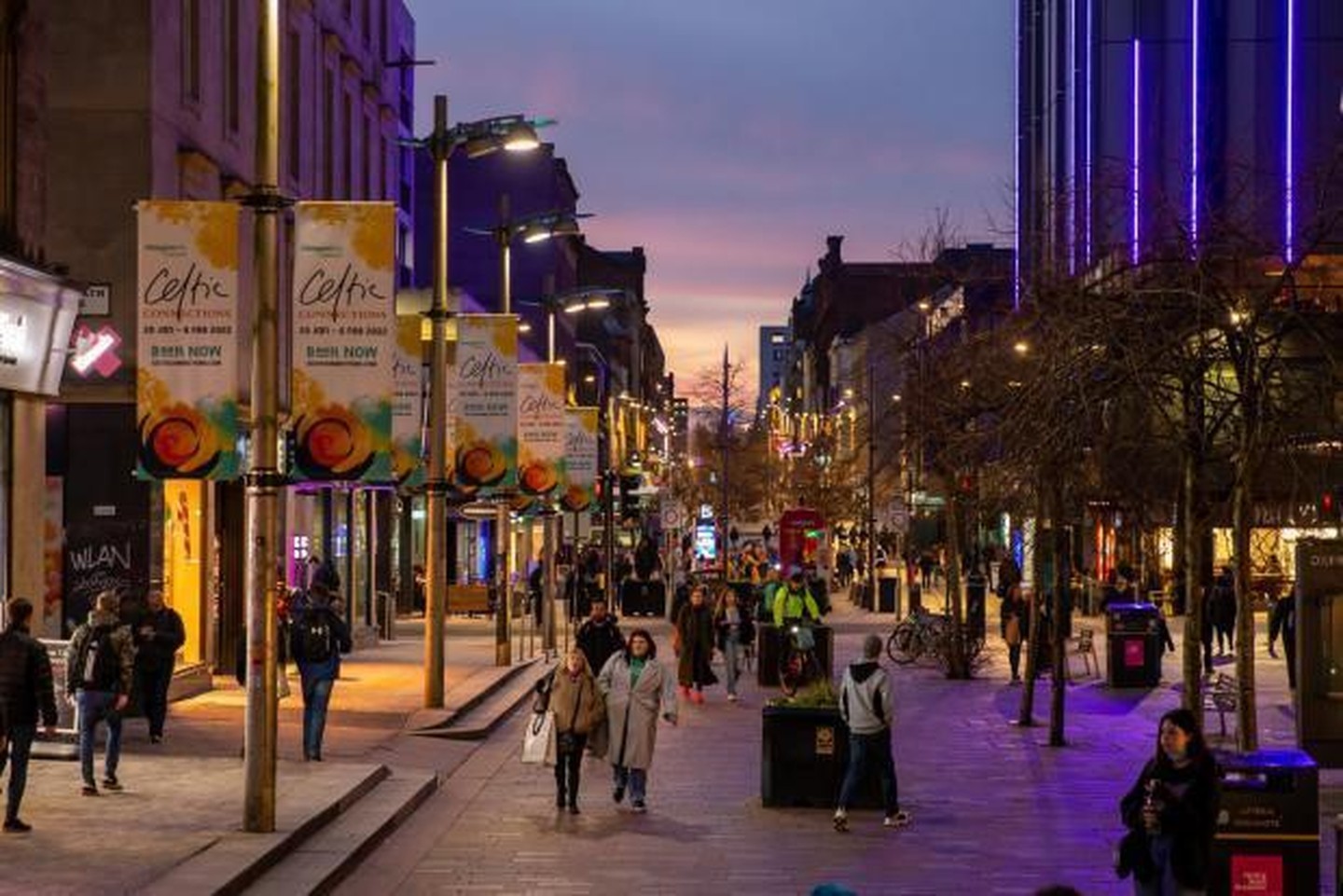 Glasgow city centre shopping street at dusk, with banners and shoppers