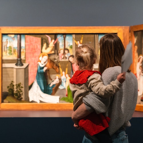 在博物馆环境中，一名成人和一名儿童正在欣赏一幅色彩鲜艳的三联画。儿童手中拿着一张白纸。