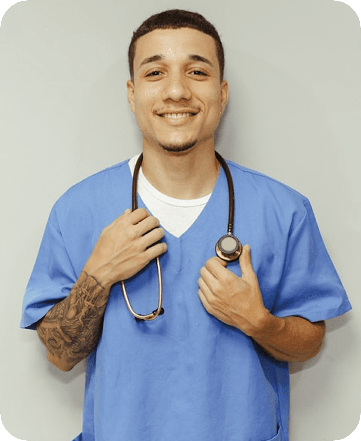A young healthcare professional in blue scrubs, with a stethoscope around their neck, stands confidently against a neutral background, smiling warmly.