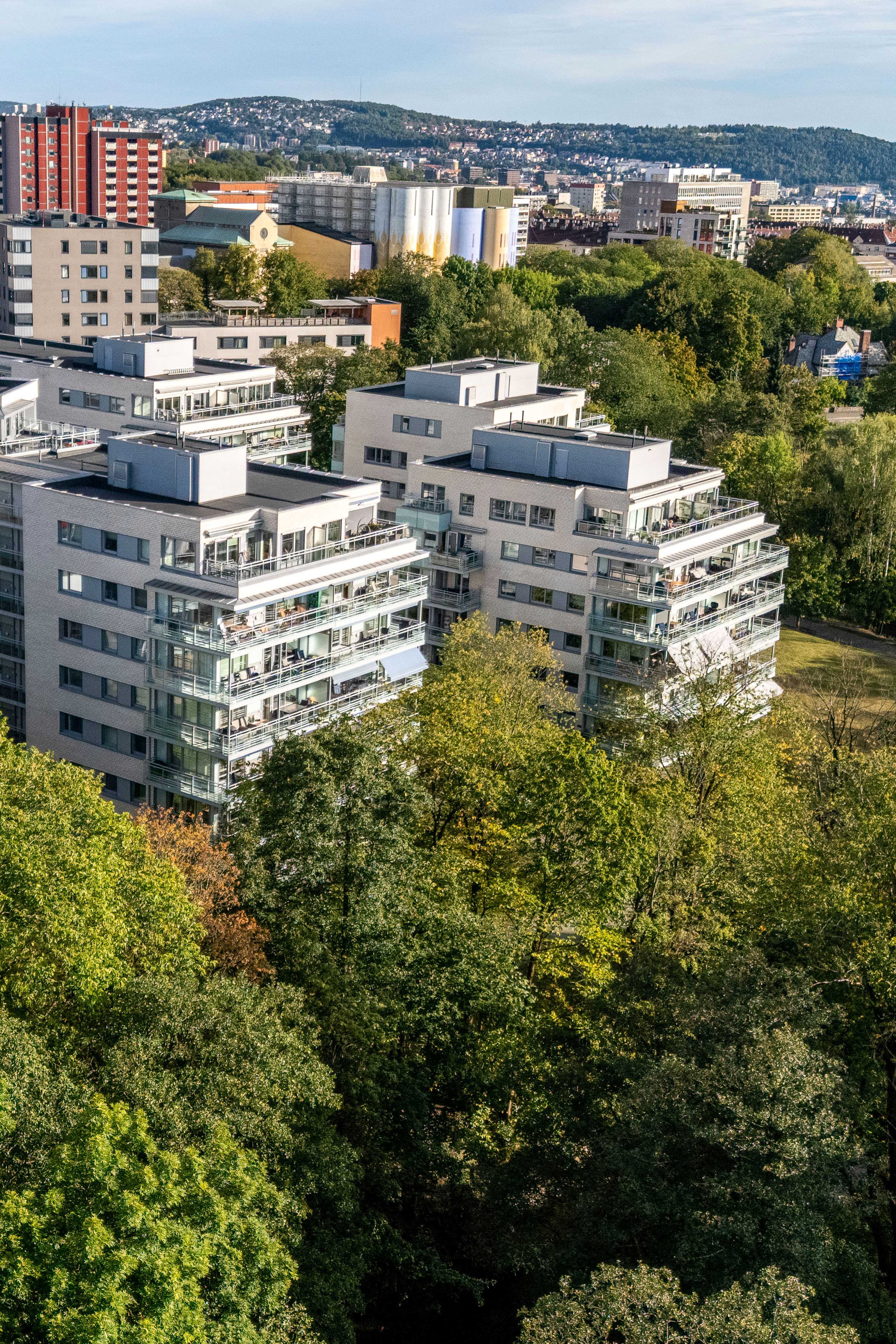 Moderne boligblokker omgitt av grønne trær med utsikt over byen