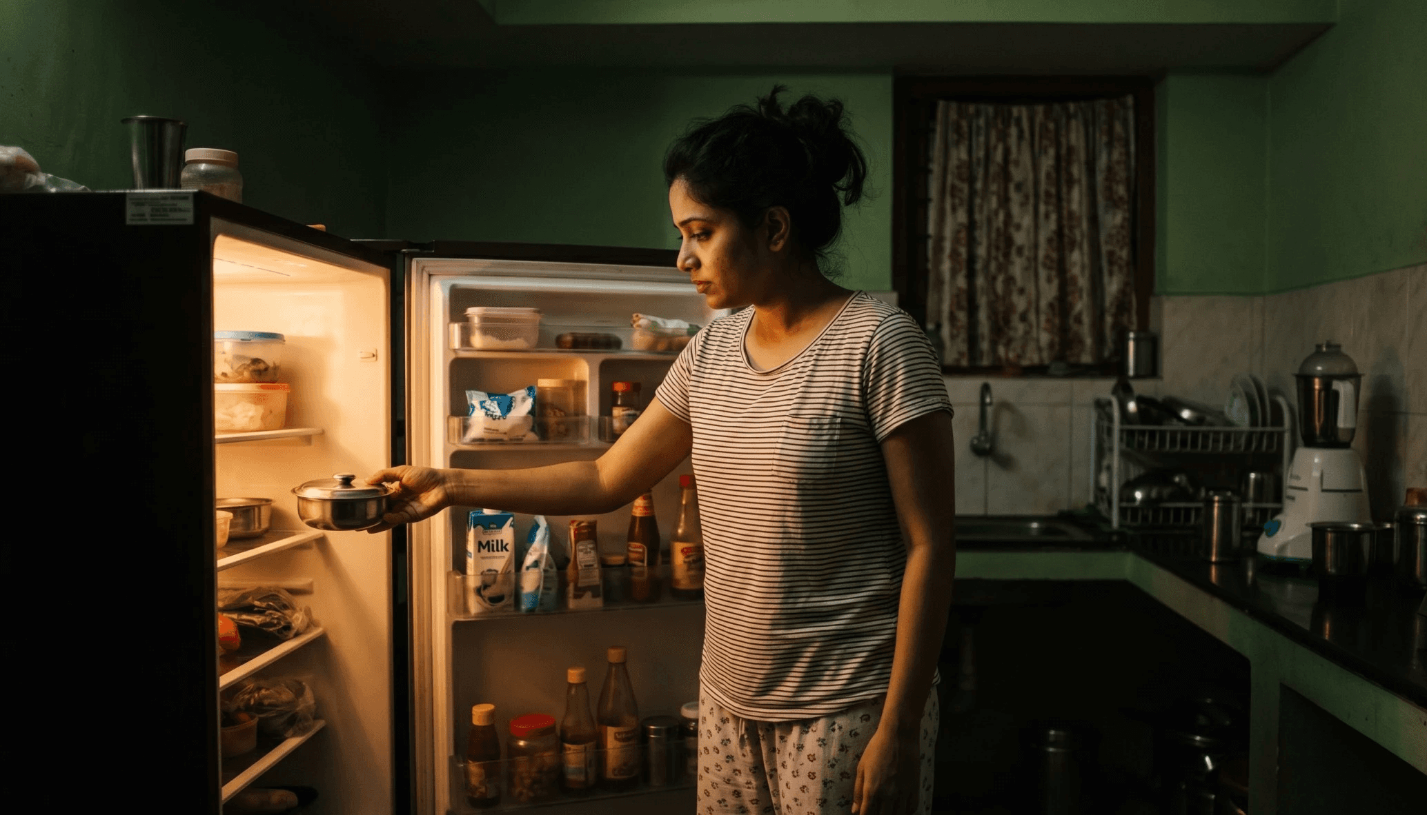 a woman getting food from fridge at night