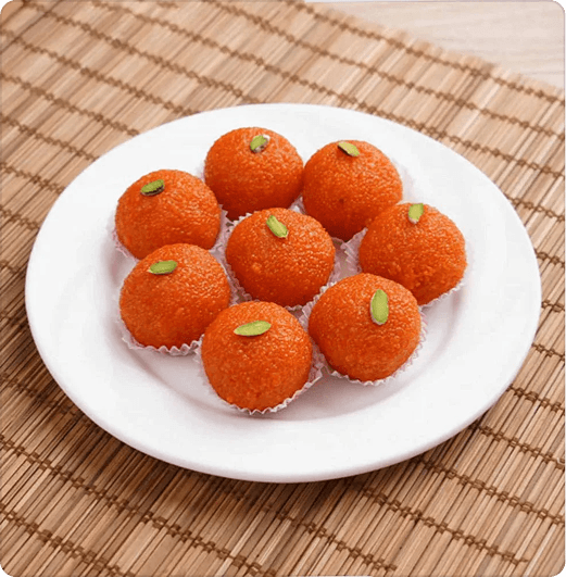 Plate of eight vibrant orange Indian Motichoor Ladoos garnished with sliced pistachios, placed on a bamboo mat.