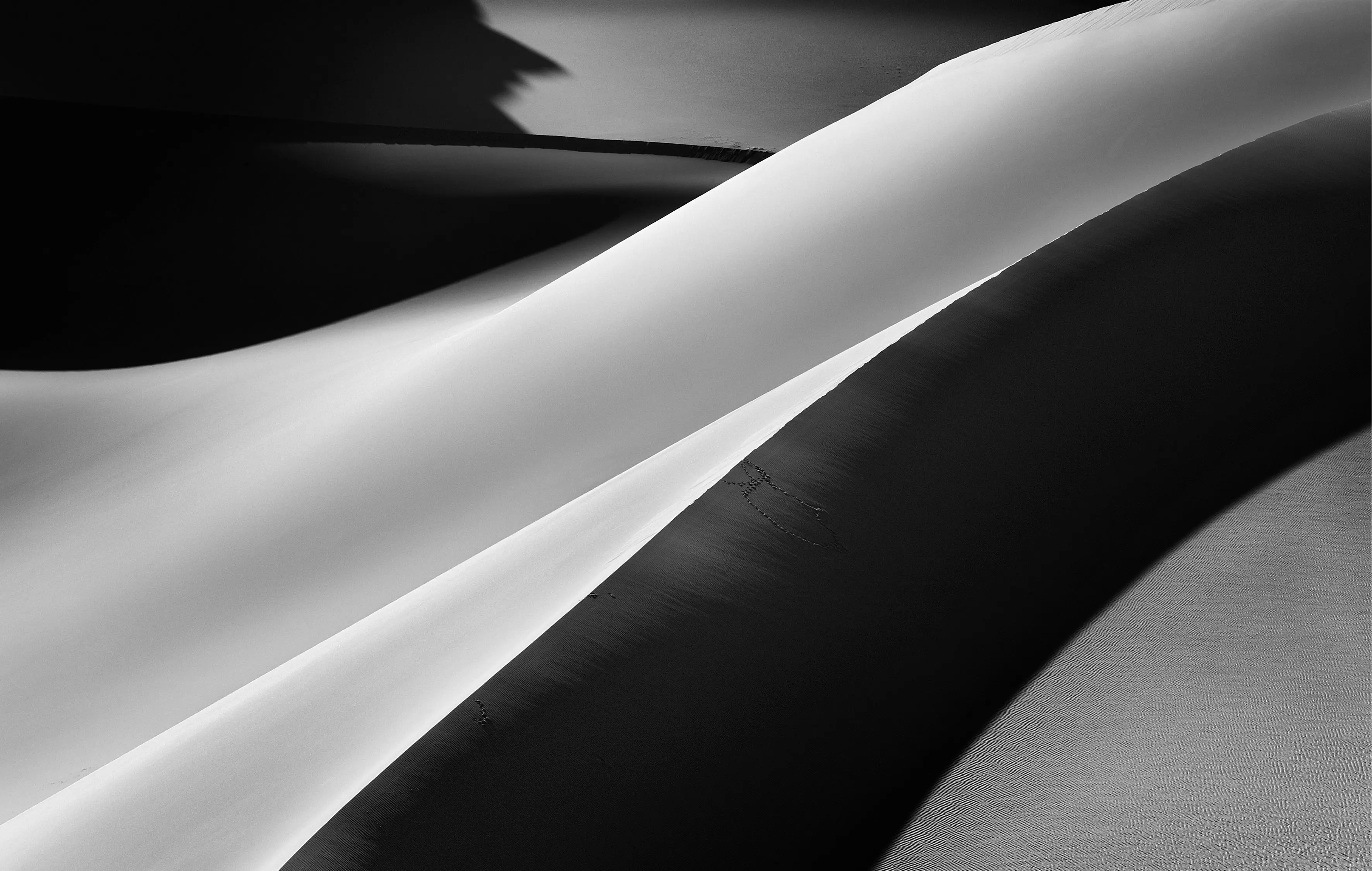 A single sharp dune ridge cutting diagonally across the frame, one face brilliantly lit and the other in deep shadow, black and white