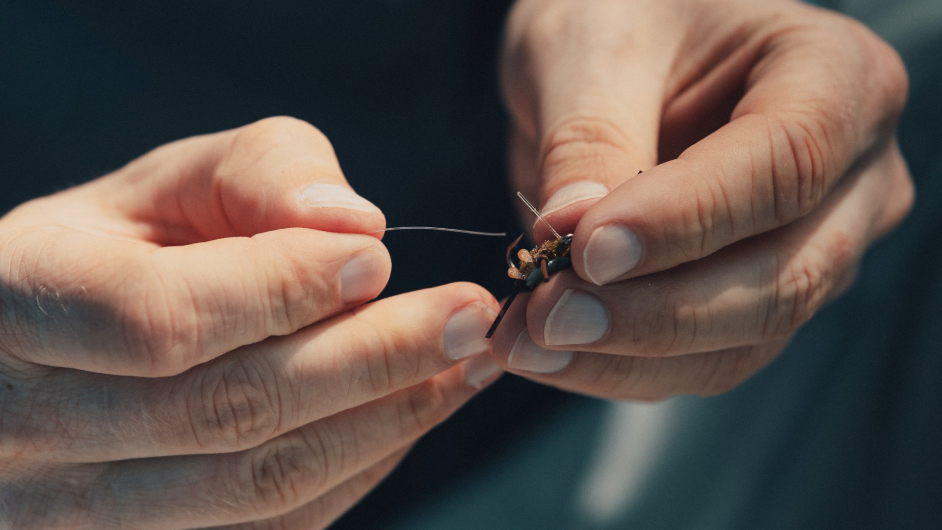 Closeup of a person tying on the Bauer Crab to monofilament tippet