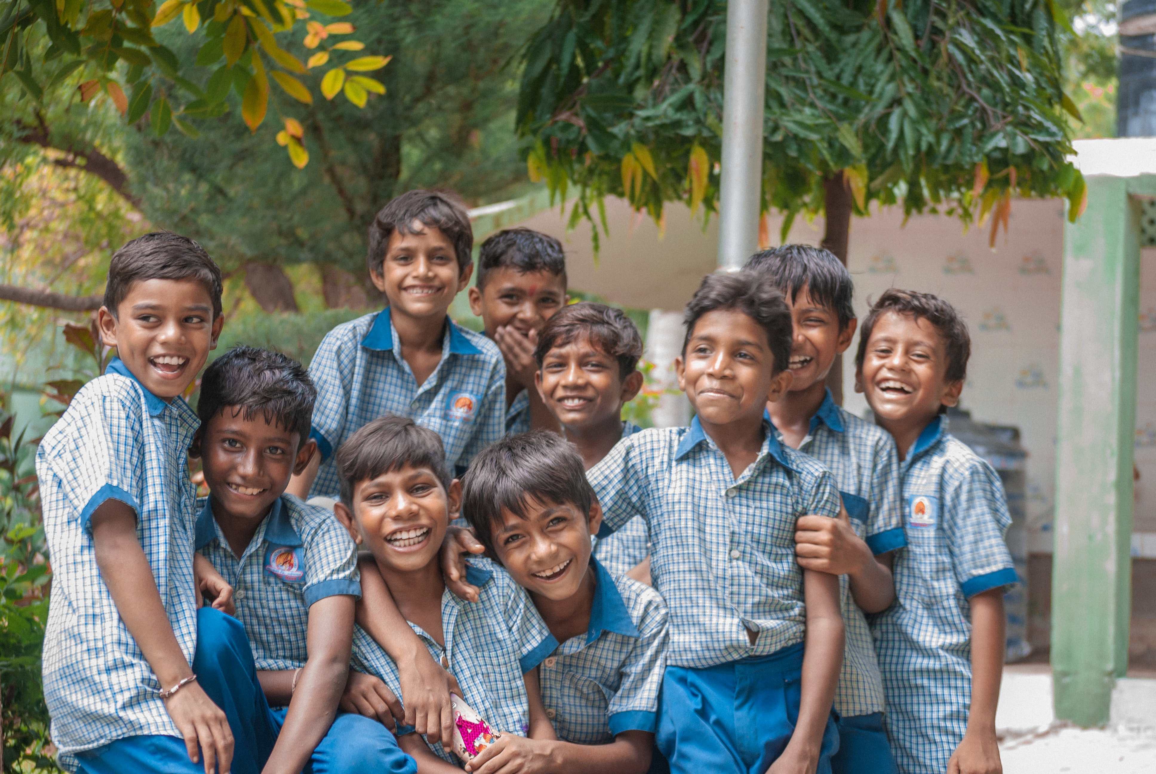 A group of cheerful Indian children in matching uniforms pose together outdoors, smiling at the camera.