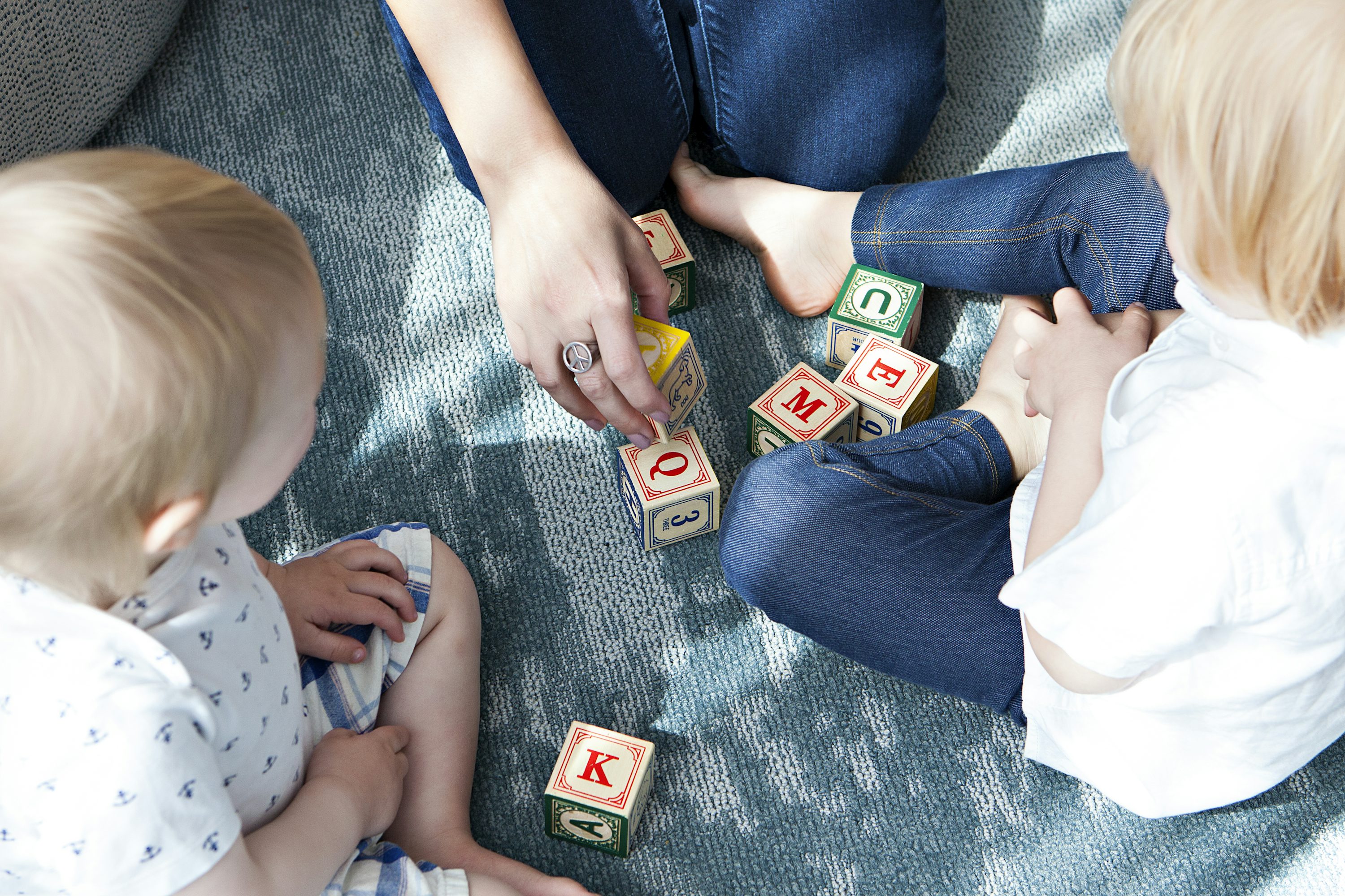 Two toddlers playing side by side with letter-block toys, practicing early language and shared attention skills.