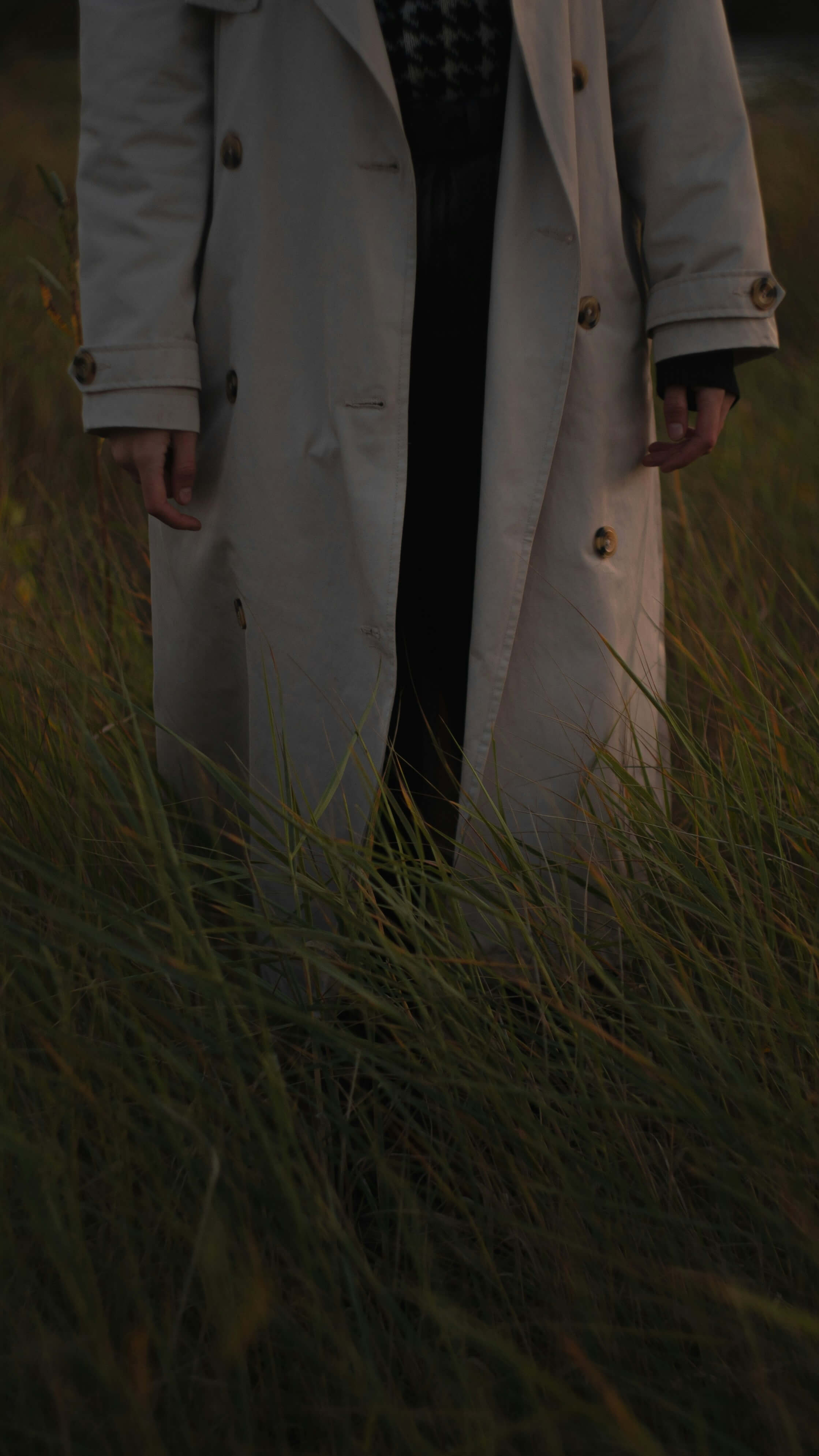 Woman standing in high grass with a beige coat