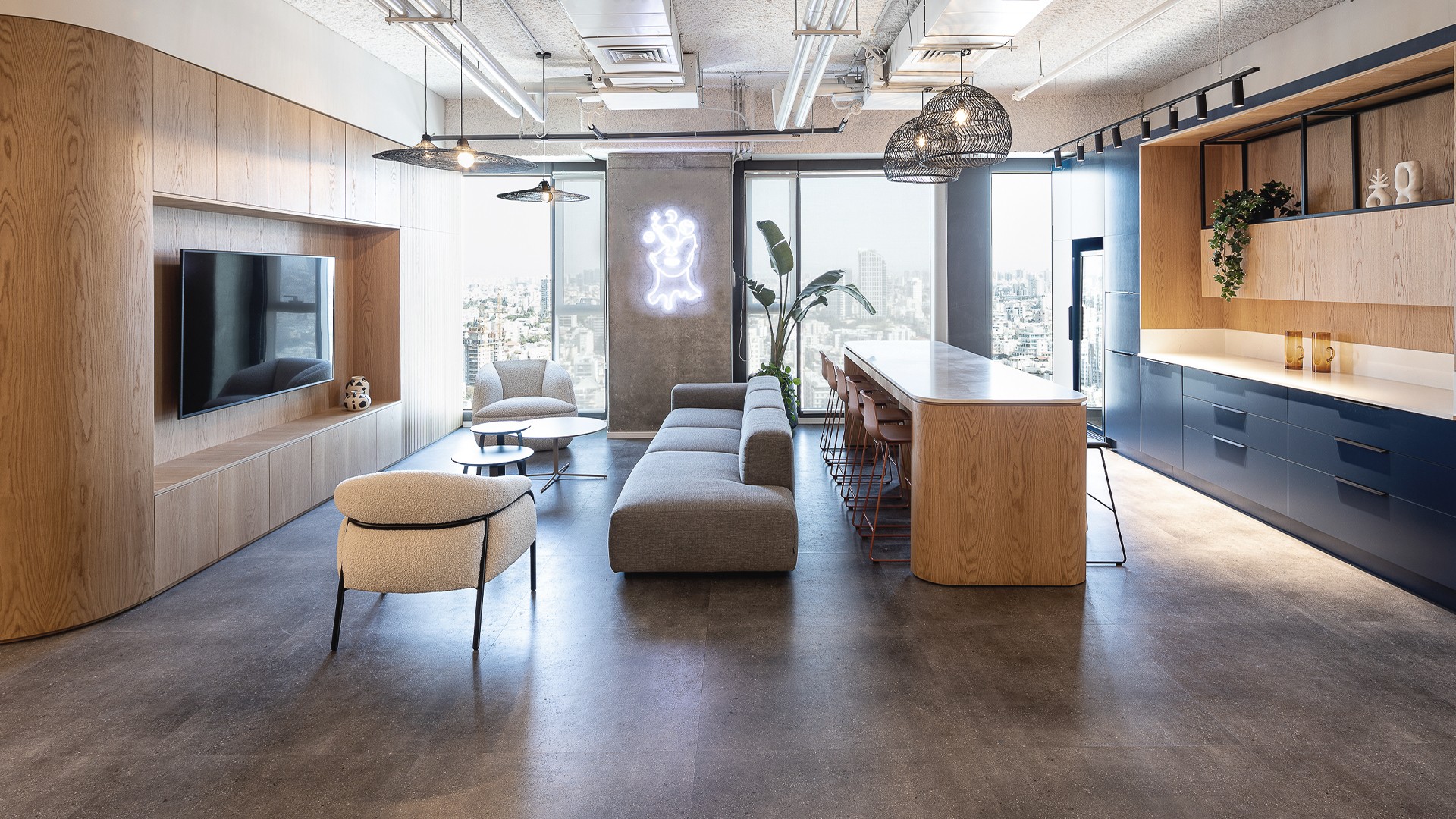 החלל המרכזי: שילוב הרמוני בין מטבח מאובזר בגוון כחול, פינות ישיבה סלוניות ונגרות עץ חמימה, היוצרים לב פועם ודינמי למשרד.