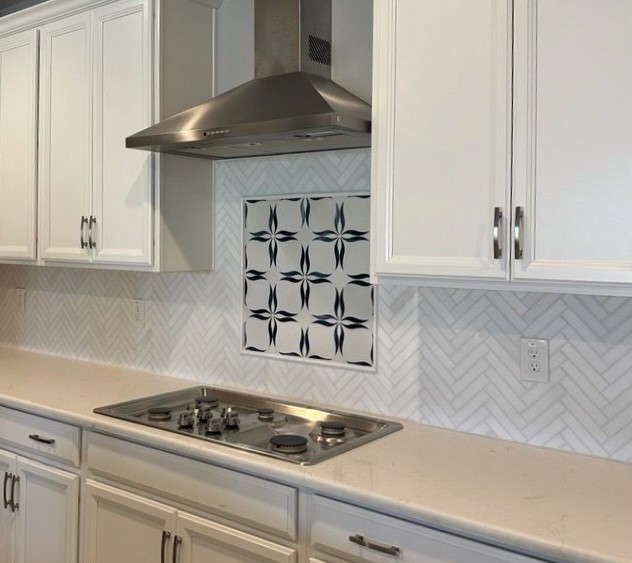 Modern kitchen with stainless steel range hood, white cabinets, and a backsplash of white herringbone tiles with a dark star-pattern centerpiece.