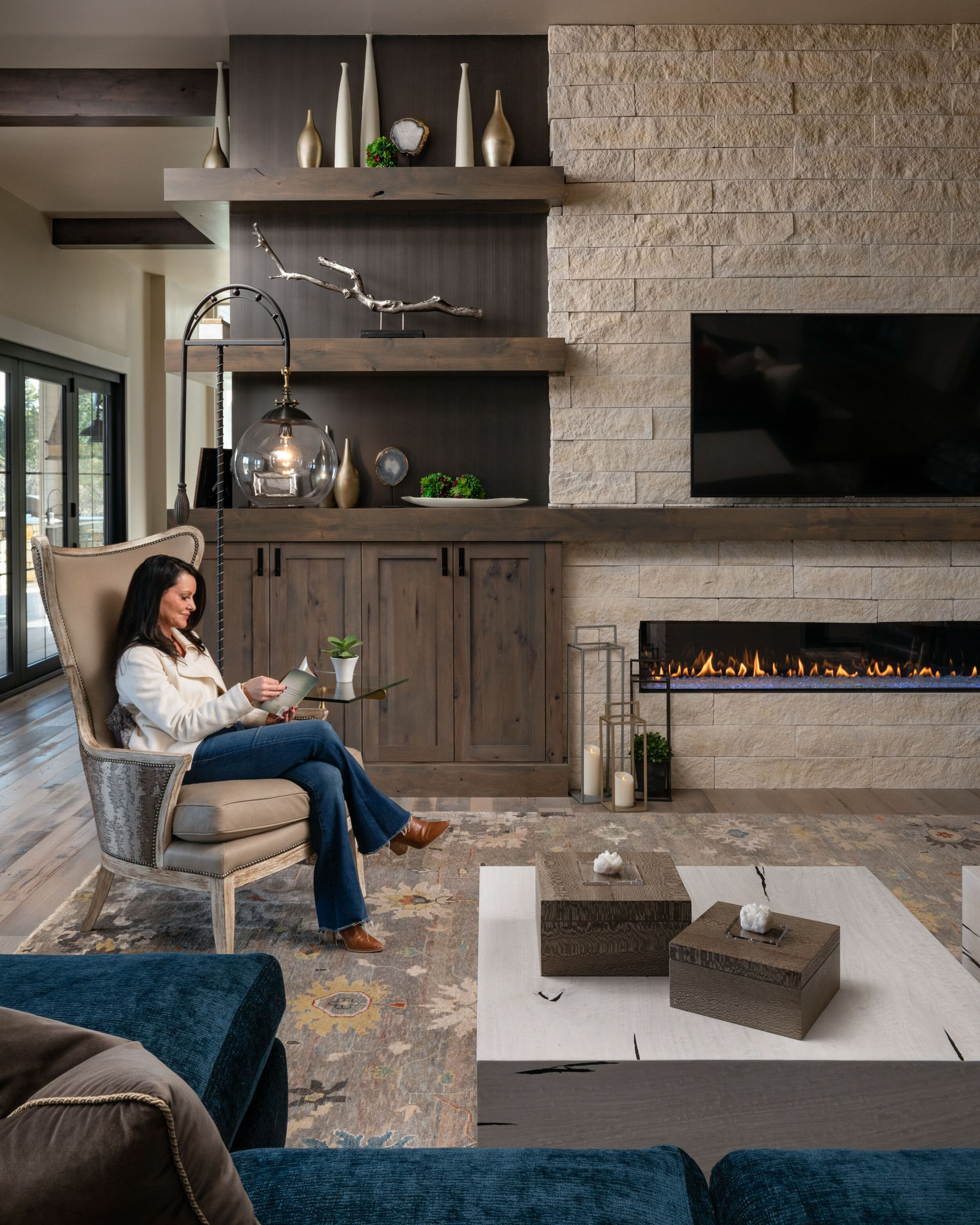 Woman reading in a high-backed chair by a fireplace.