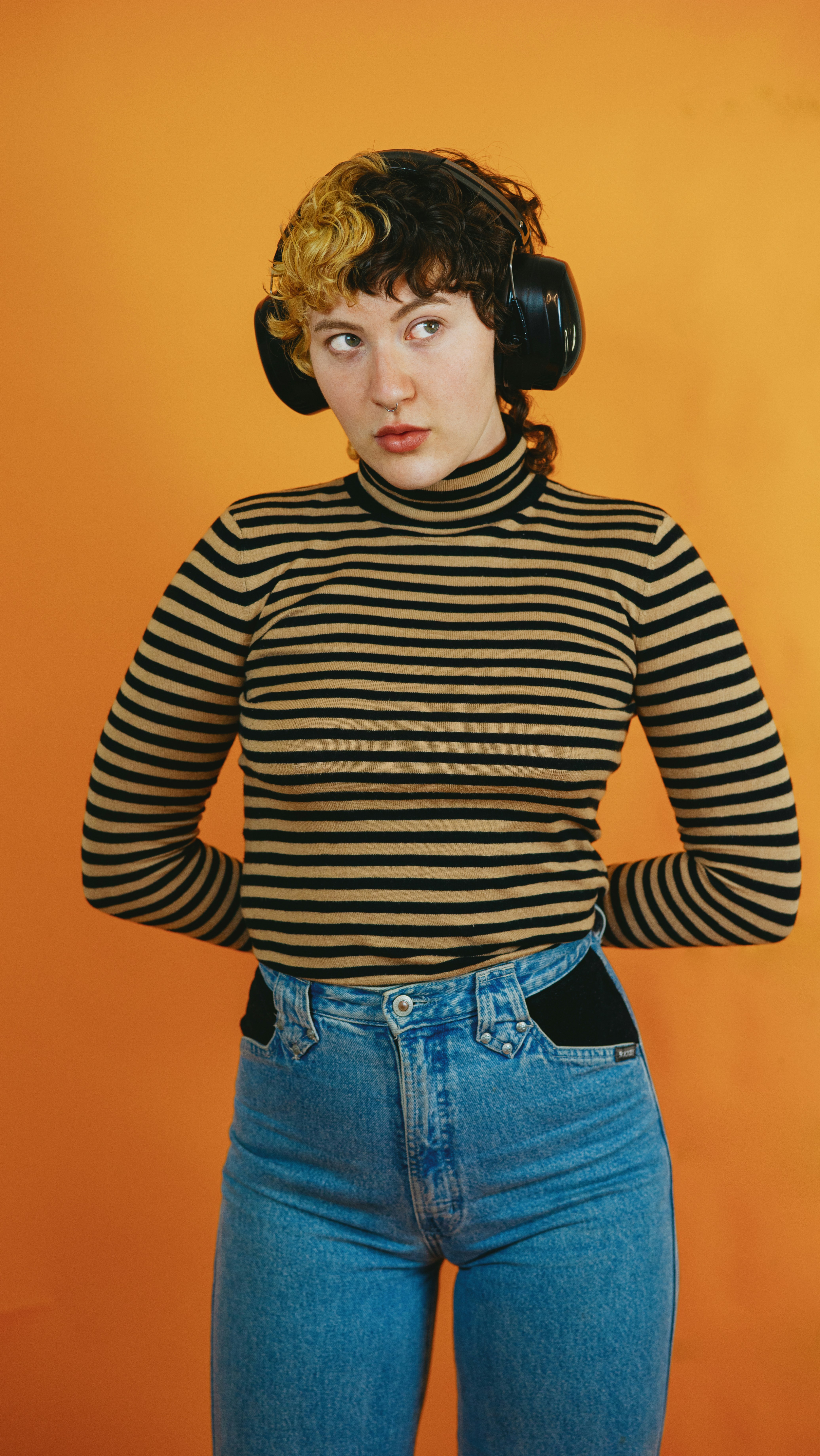 Young female wearing headphones and a striped top against an orange background