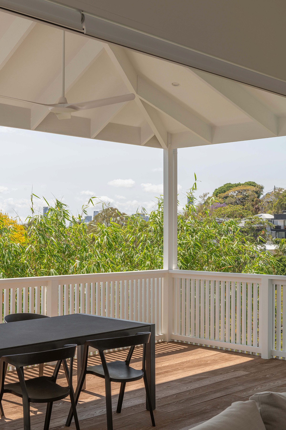 Covered timber deck with white balustrade, outdoor dining setting, and leafy suburban views beyond.