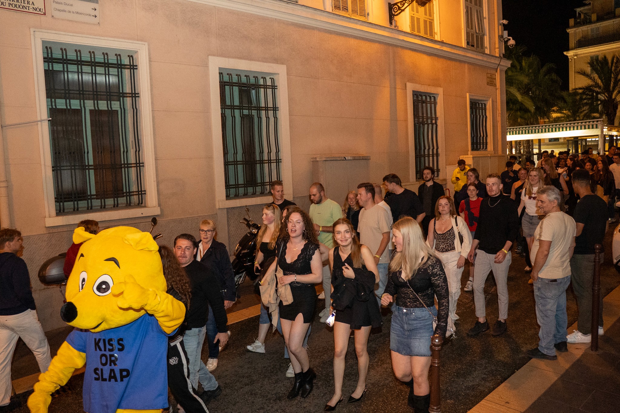 A nighttime scene in Vieux Nice with narrow streets, warm lights, lively bars, and groups of people walking between venues.