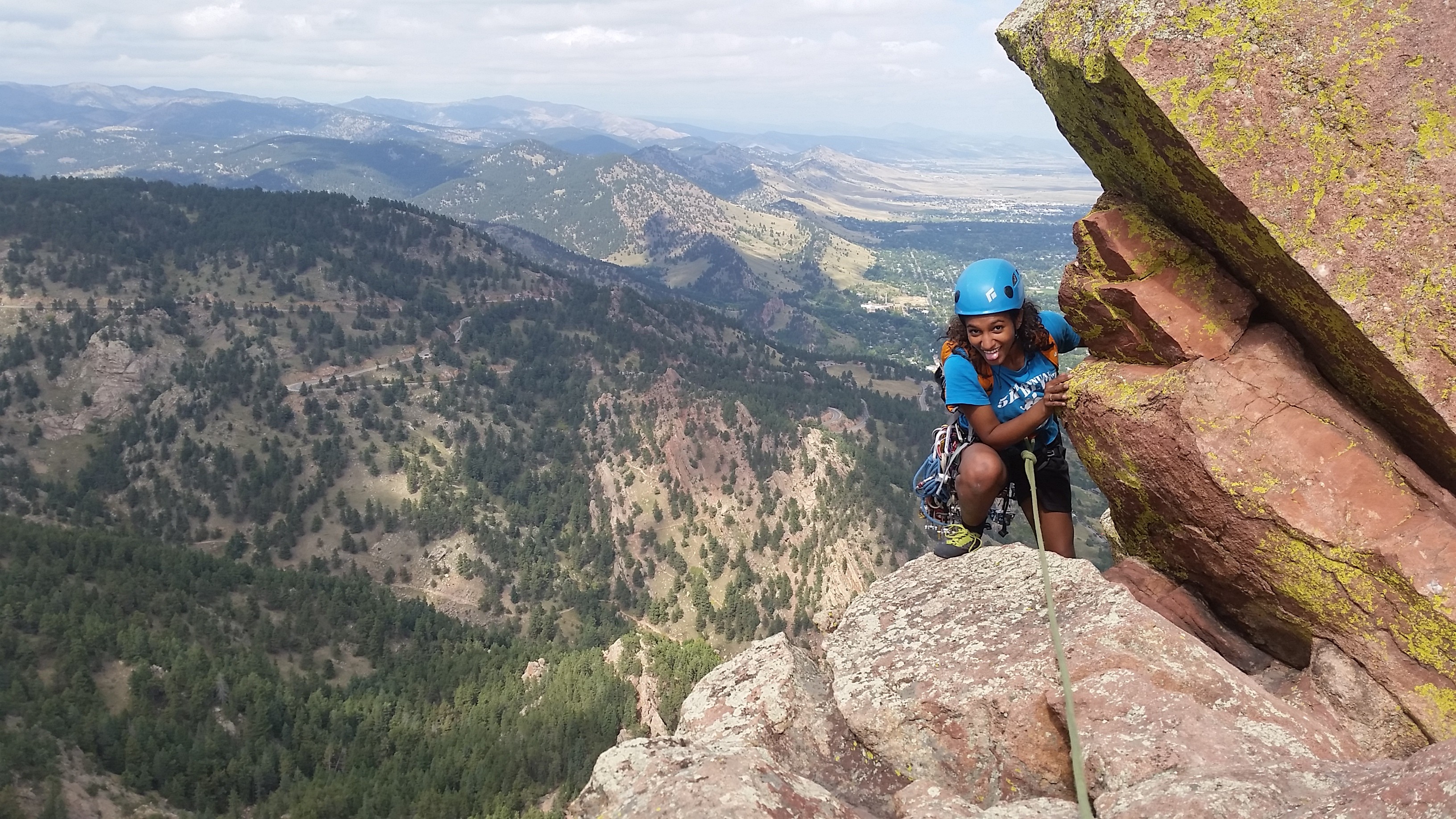 Climber sticks out their tongue as the climb across first flatiron with mountains spreading to the horizon