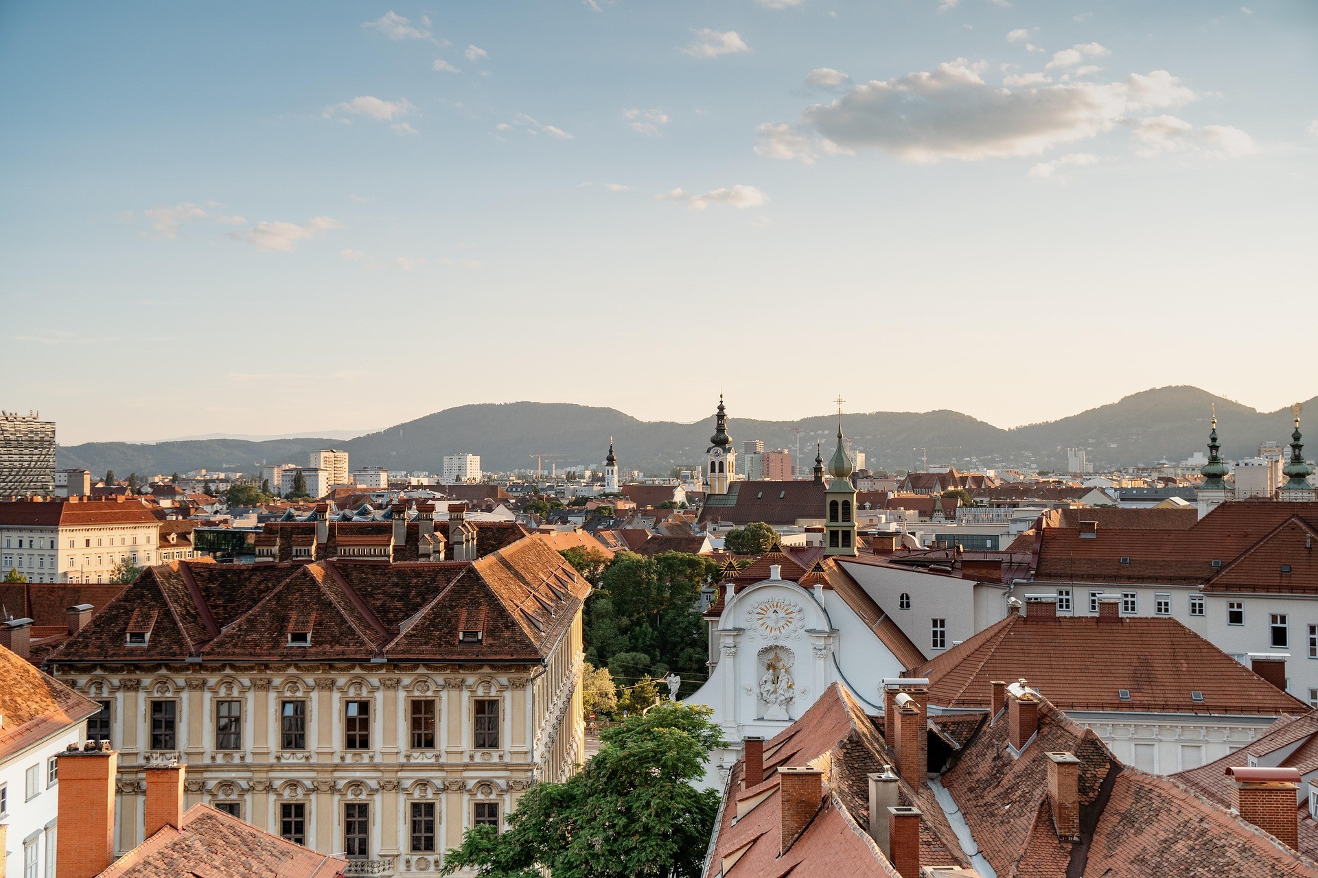 Blick auf Graz mit roten Dächern und Bergpanorama im Hintergrund bei Sonnenuntergang.