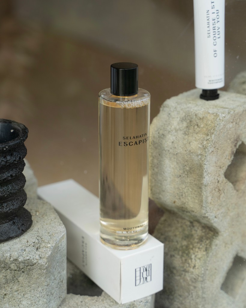 A bottle of Selahatin Escapist mouthwash on top of a white box, with a textured stone backdrop and a black ceramic holder.