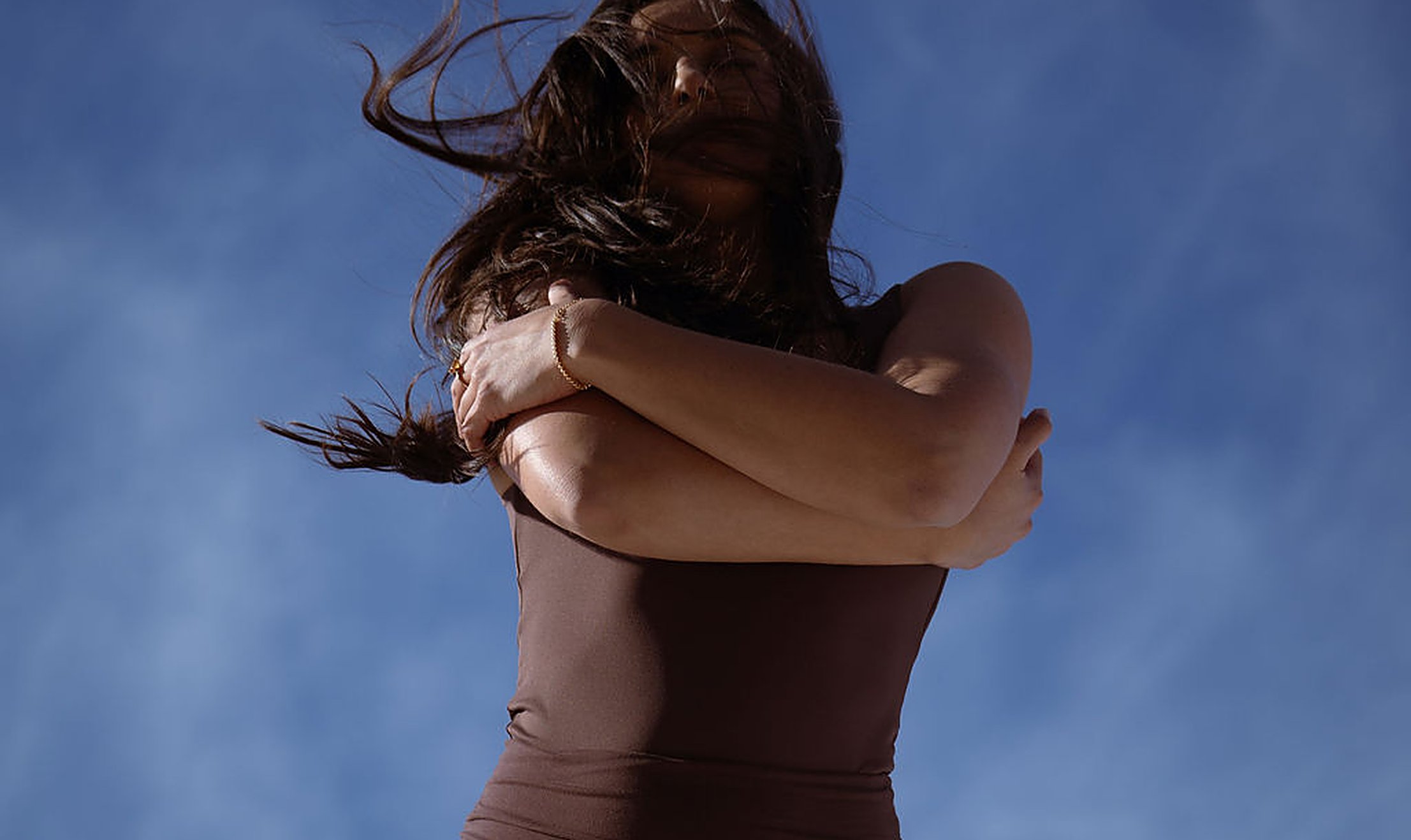 Woman wrapping her arms around herself against a soft blue sky, self-soothing when stress and low libido take hold | My Temple