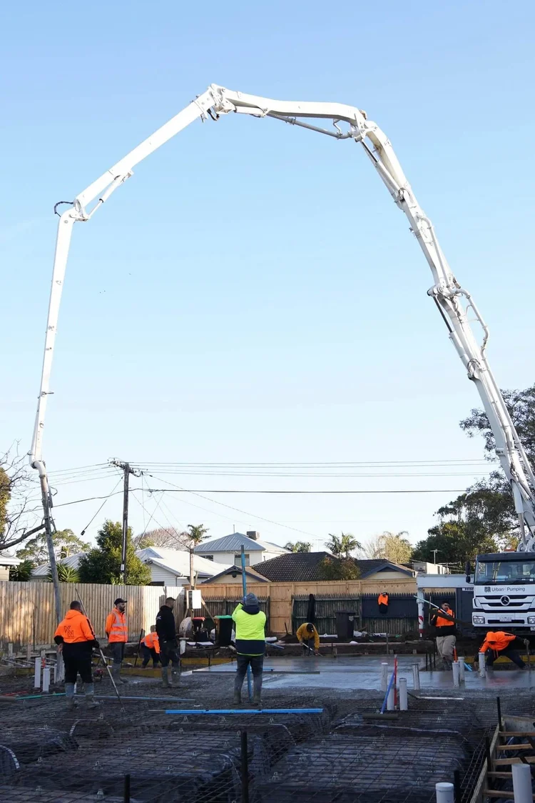 Construction site with workers using concrete pump truck for foundation pouring.