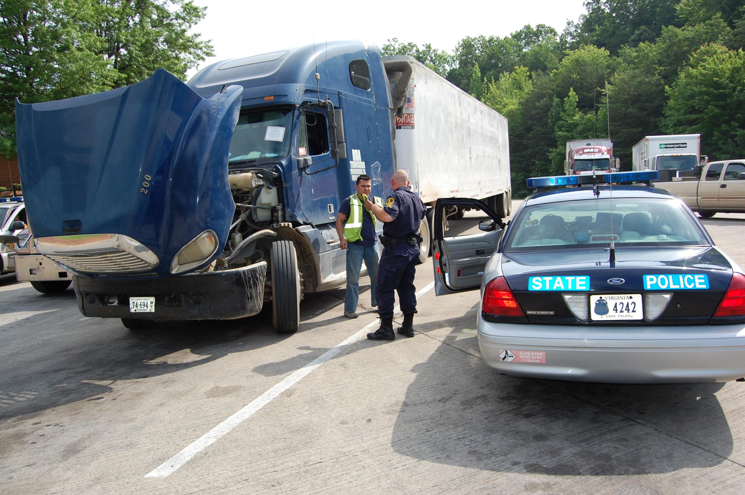 Police officer inspecting a semi-truck parked at a weigh station.