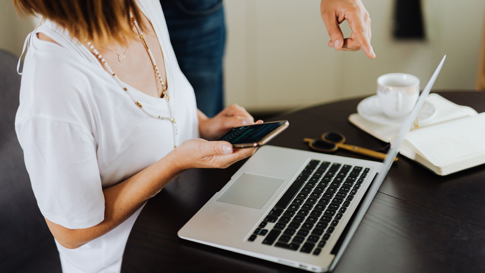 Business professionals collaborating using a laptop and smartphone over coffee in an office setting.