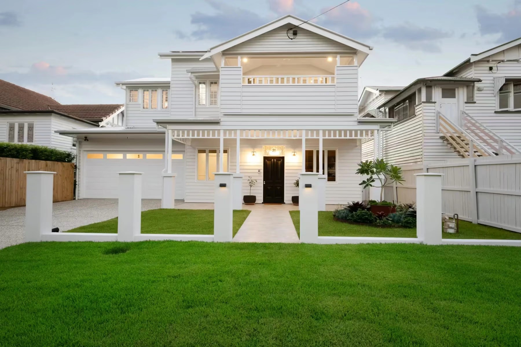 Front facade of a renovate Queenslander home by Invilla Architecture, featuring traditional gables, a modern double garage, and a manicured green lawn.