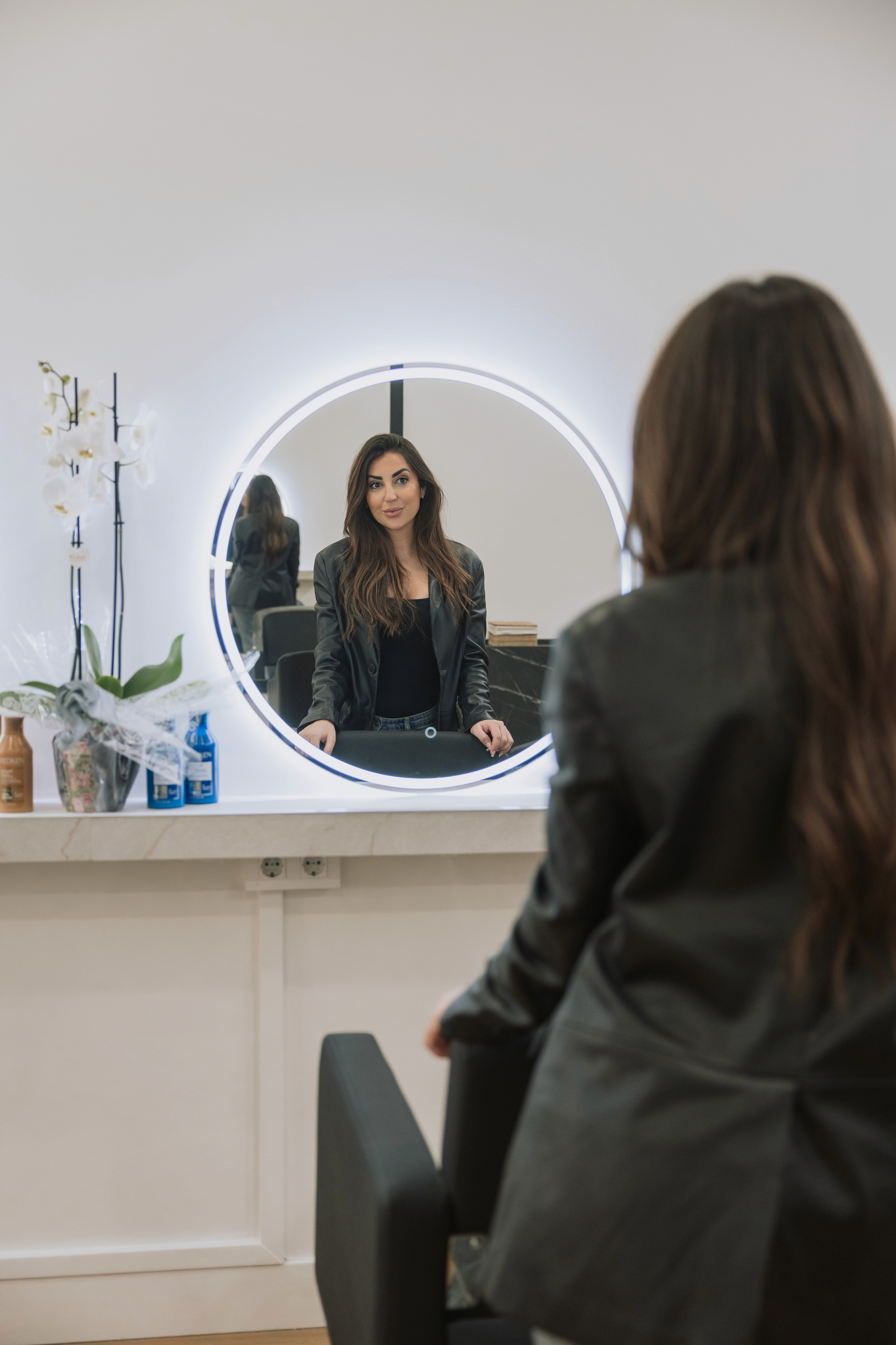 A woman lying down in a spa setting, relaxing with her eyes closed. Sunlight streams through blinds, casting striped shadows on her face. The scene conveys a sense of serenity and well-being.