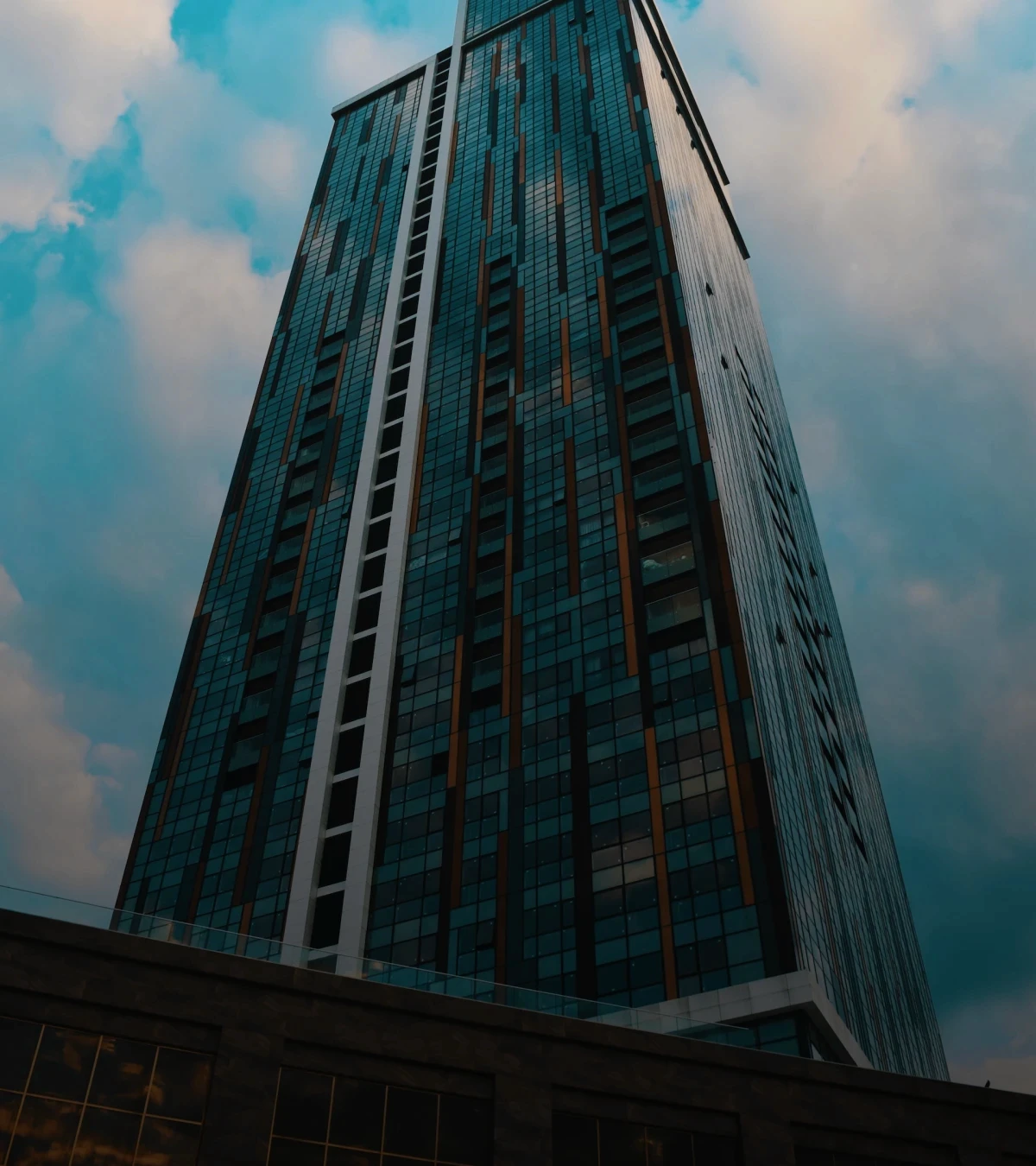 imagem de um da frente de um edifício empresarial, foto tirada de baixo para cima. Céu azul e com nuvens de fundo na imagem.