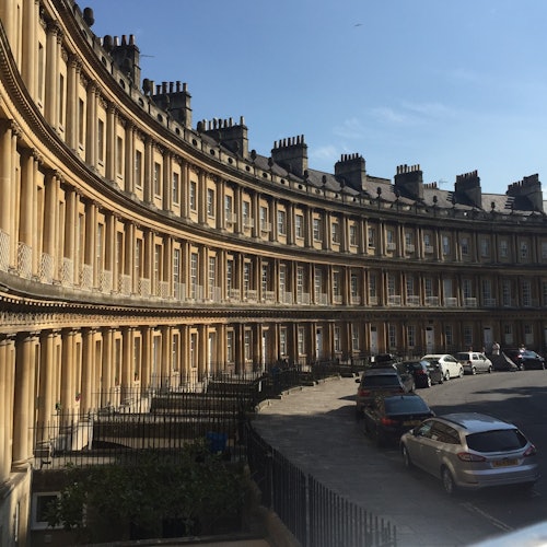 一排弯曲的多层黄色石头建筑,屋顶冒着烟囱,街道上停着几辆车。天空湛蓝而晴朗。