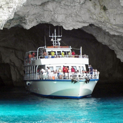 一艘滿載人員的船進入一個大洞穴，清澈的藍色水面與洞穴的黑暗內部和岩石天花板形成對比。