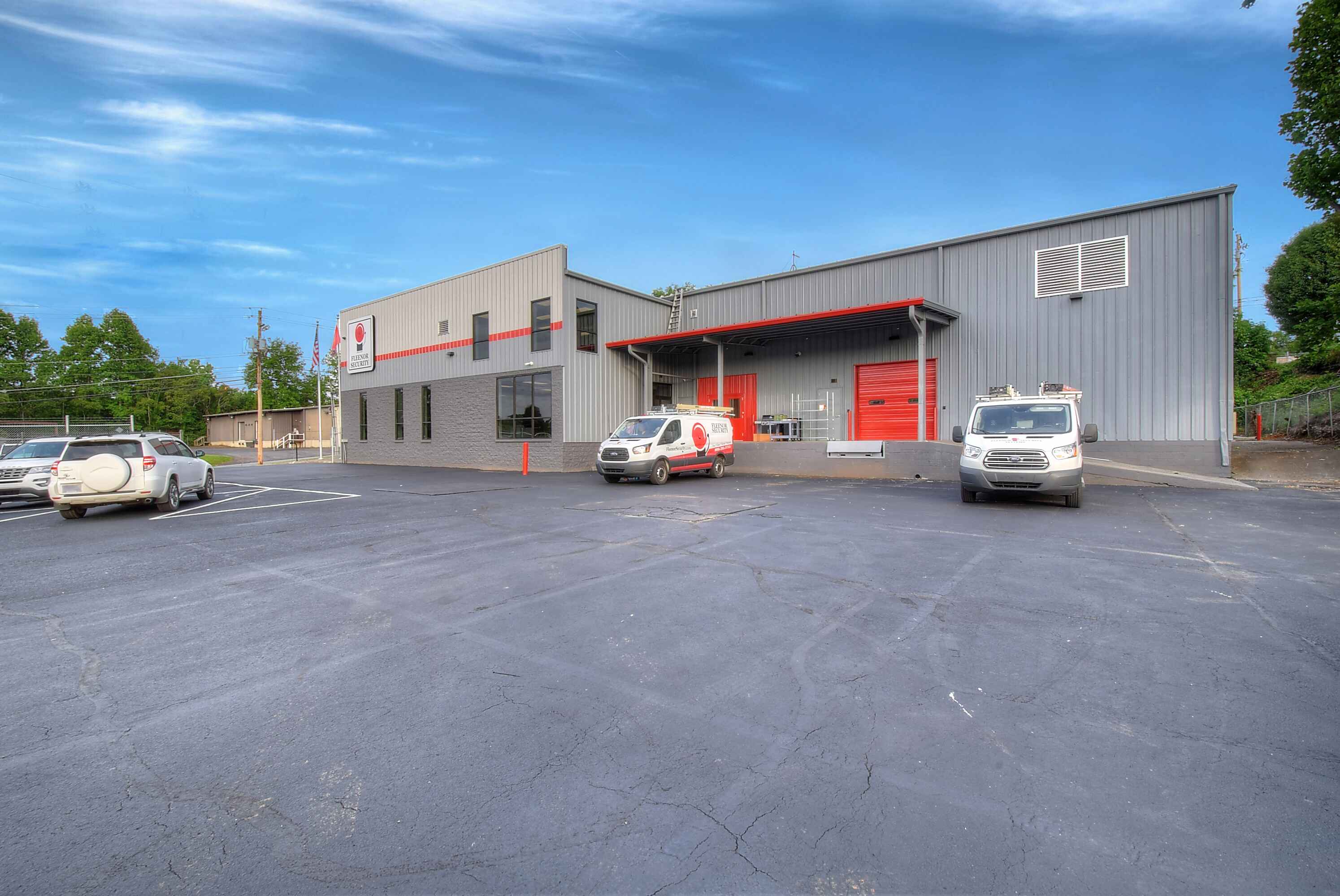 A large gray building with red accents, surrounded by parked cars and a clear blue sky.