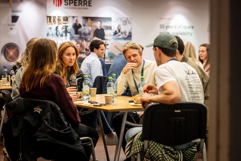 A group of people sitting around a table engaged in conversation in a casual setting.
