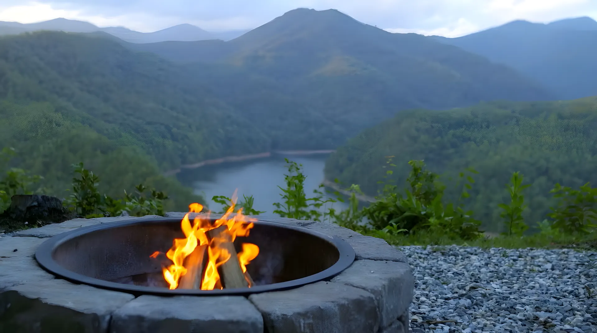 Fire burning in a stone fire pit with Fontana Lake and green ridges behind