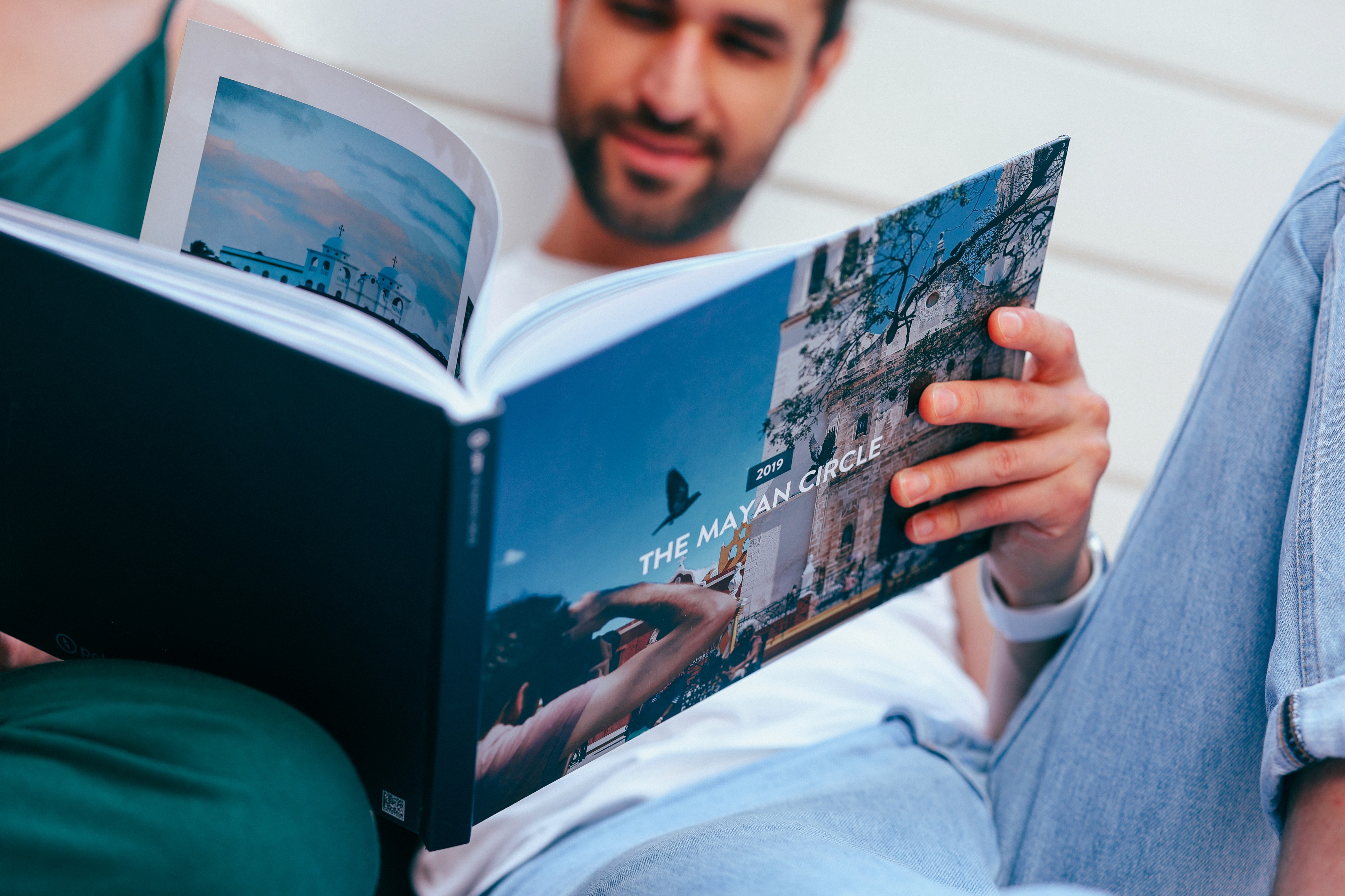 A person reclining, flipping through a Polarsteps Travel Book titled "The Mayan Circle."