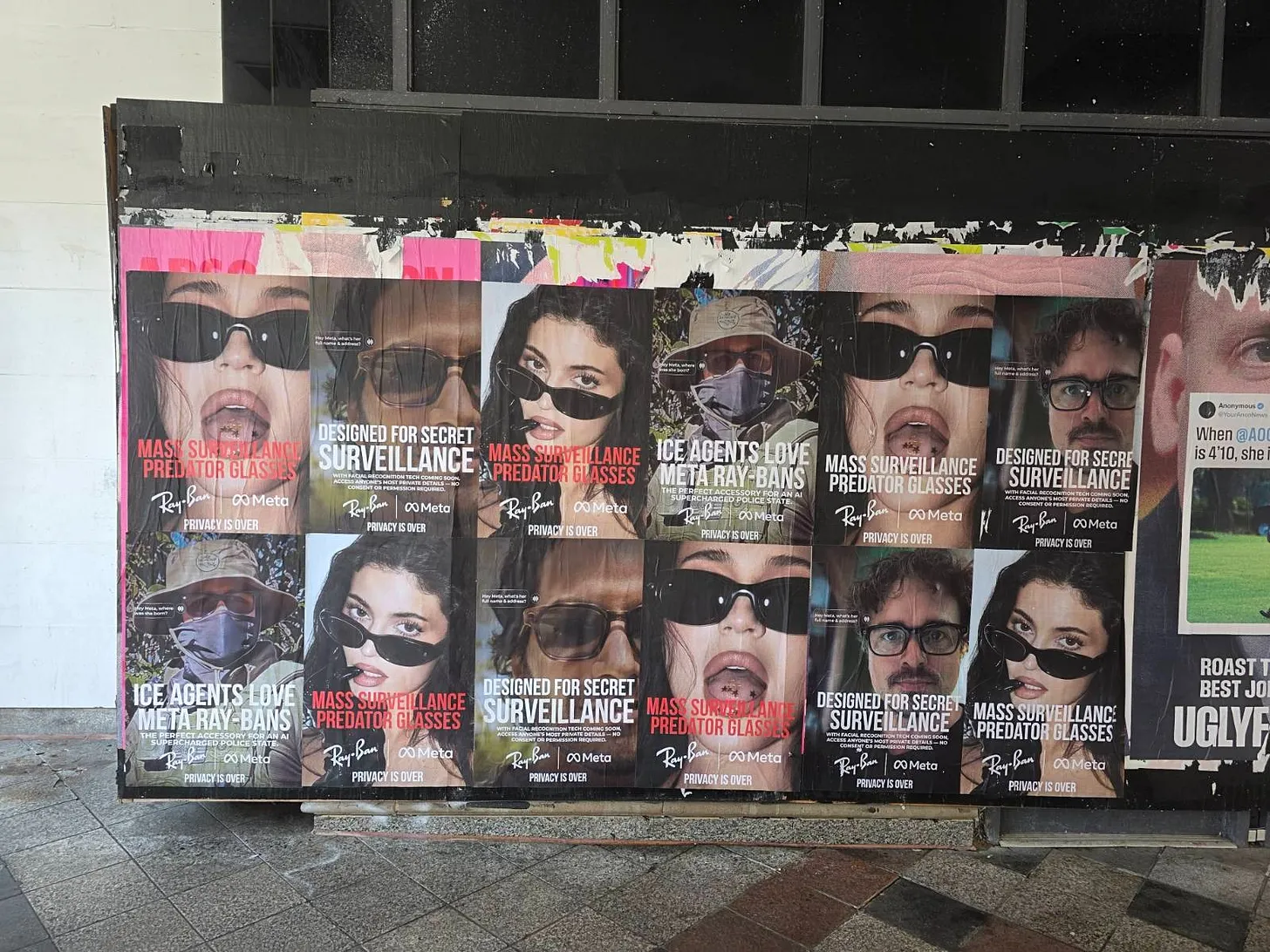 Wall covered with parody Ray-Ban Meta posters criticising surveillance and privacy loss, including slogans “Mass surveillance predator glasses” and “ICE agents love Meta Ray-Bans.”