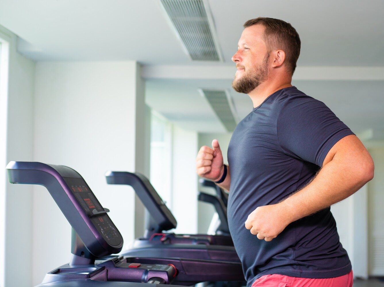 plus-sized man smiling while he runs on the best treadmill for weight loss at the gym as he enjoys his workout