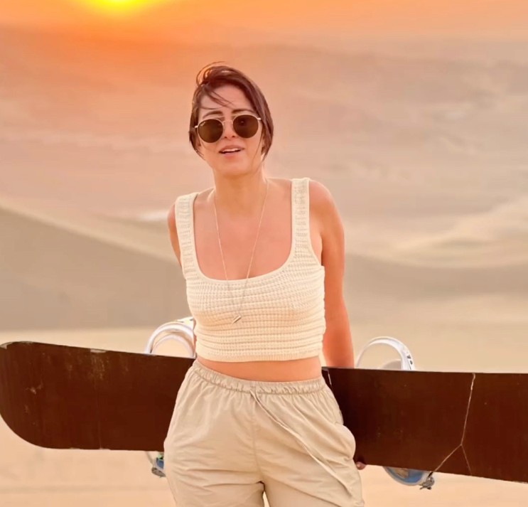 Young man with brown hair and blue eyes in an urban setting with graffiti background, wearing a dark jacket and chain necklace.