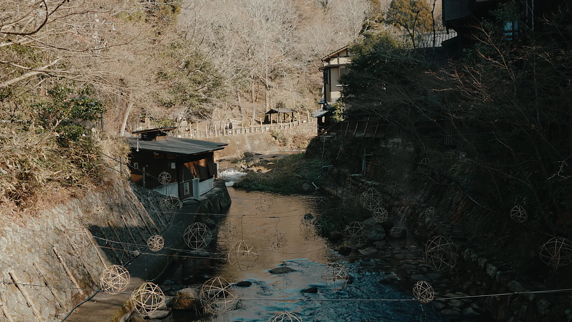 The river channel between inns at Kurokawa Onsen in winter, a riverside bathhouse on the bank