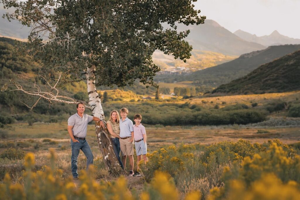 Family of four standing beside a tree in an autumn mountain meadow