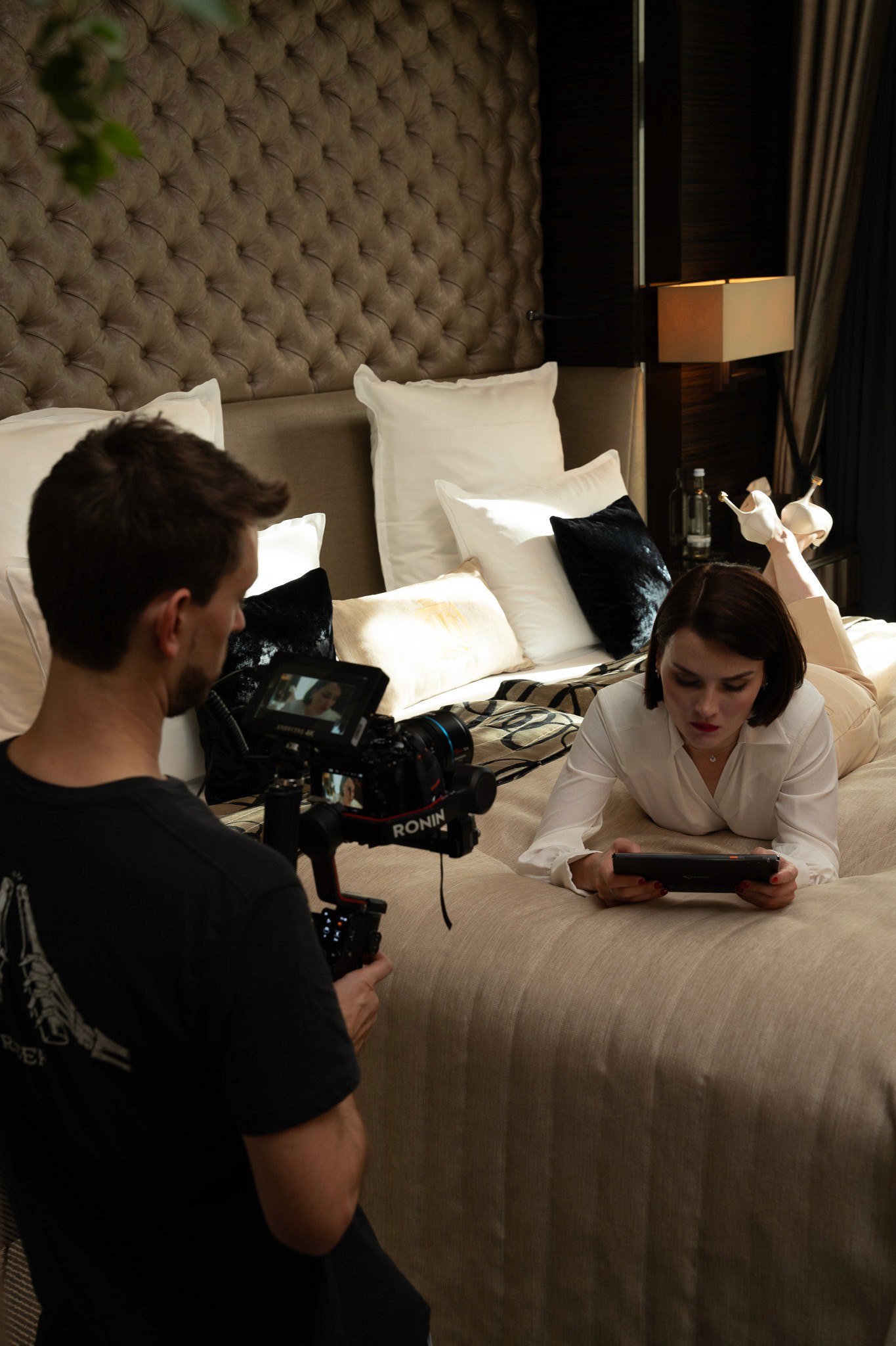 Videographer filming a model on a bed, reading her tablet in a hotel room