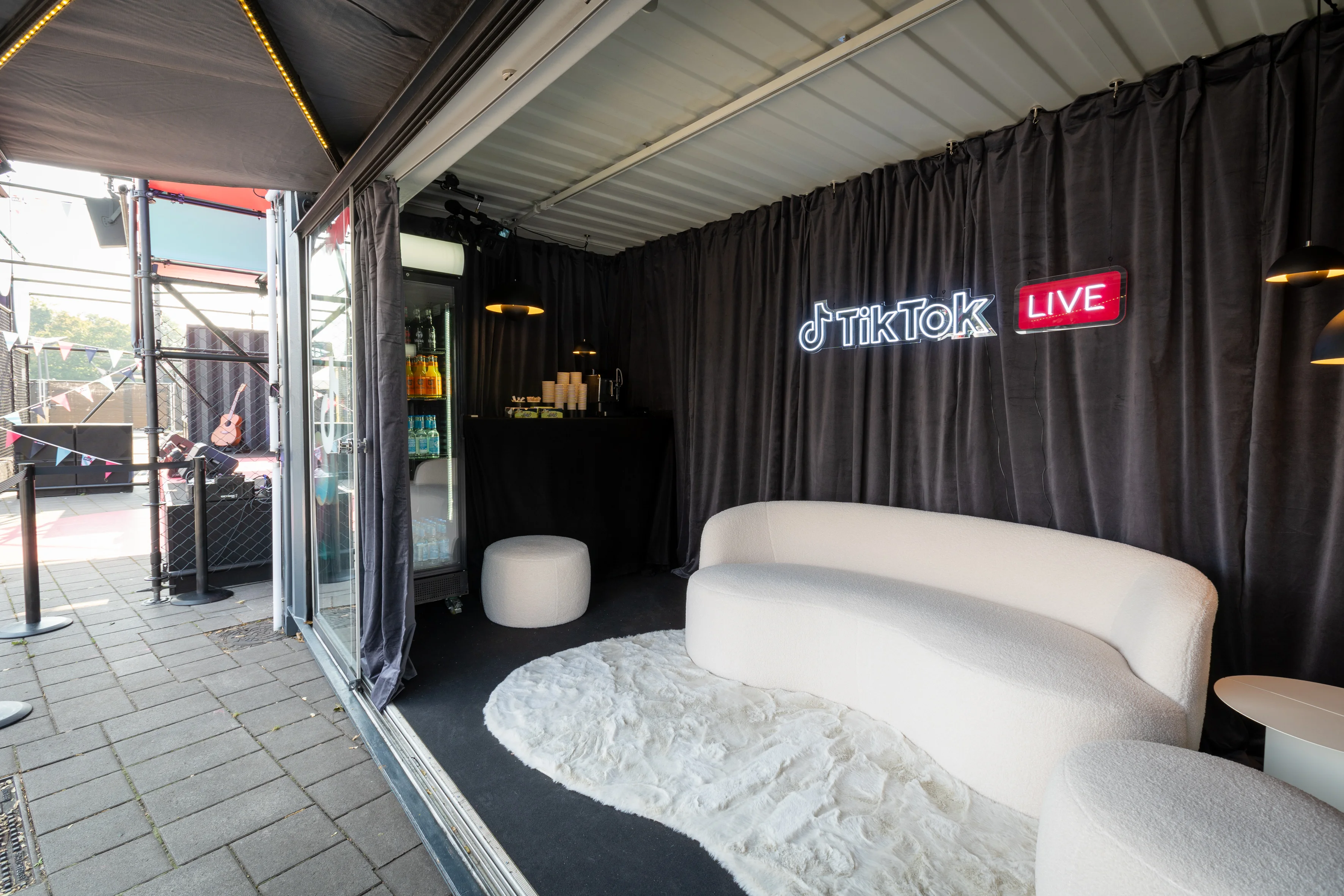 Container lounge with white bouclé sofa, fluffy rug, drinks fridge and glowing TikTok Live sign.